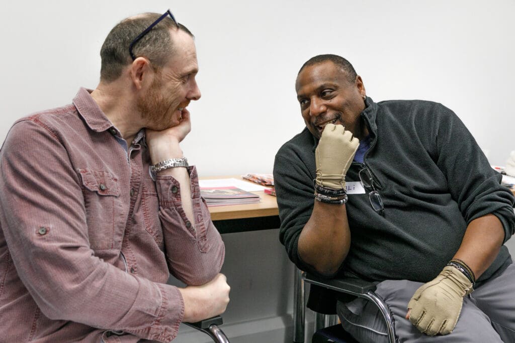 Two mentors involved in a conversation. Both are smiling - one is wearing a red checked shirt and the other a black fleece.