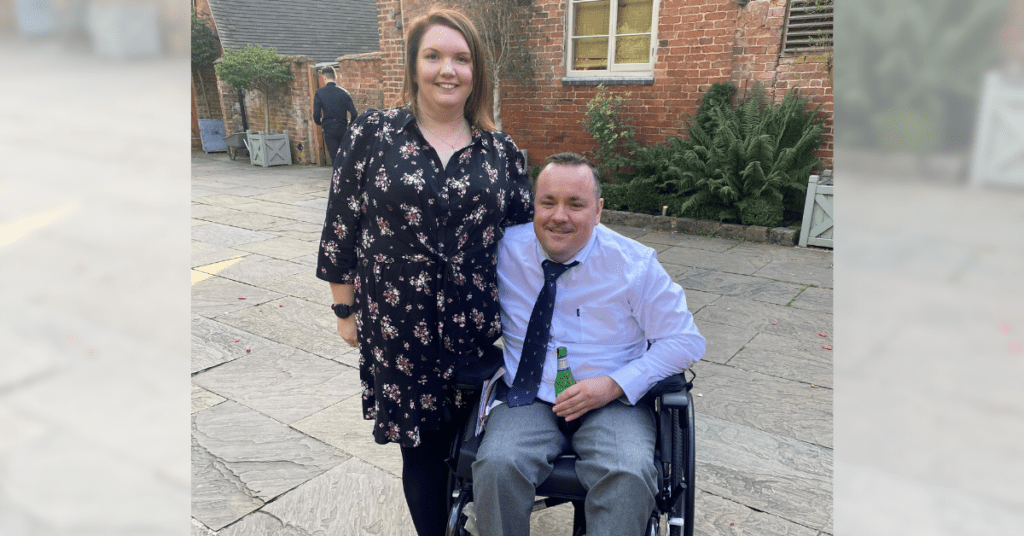 A picture of Karen and her partner who are both smiling on a summers day. Karen accessed our family mentoring service after her partner sustained a spinal cord injury.