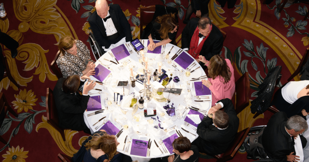 Arial view of one of the tables laid at City Dinner. The table is circular with nine people sat on it and purple brochures at each place setting.