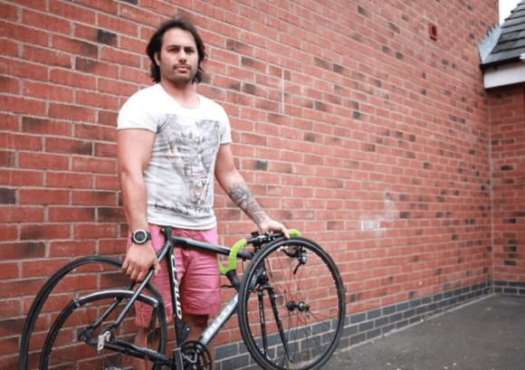 Adrian posing by a wall with a bike