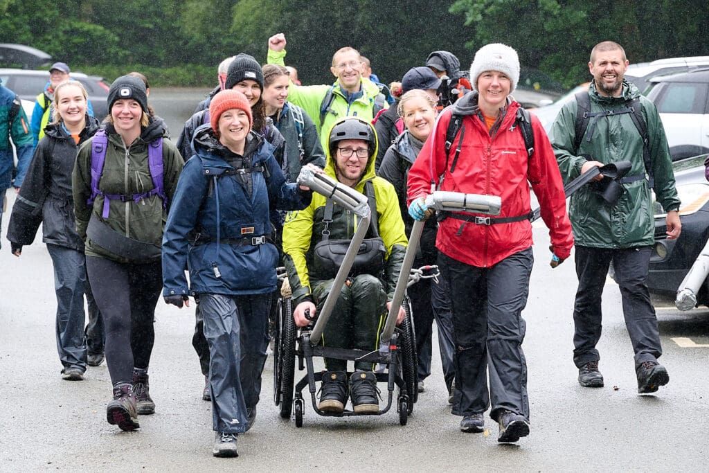 Mark in his adapted wheelchair surrounded by his team, all wearing mountain gear and smiling