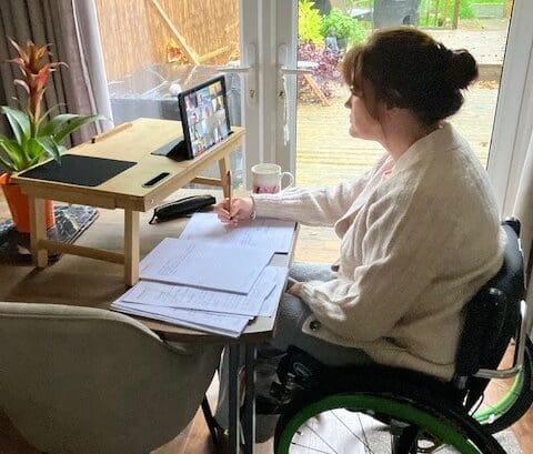 Woman sitting at her desk in her wheel chair, taking notes at home.