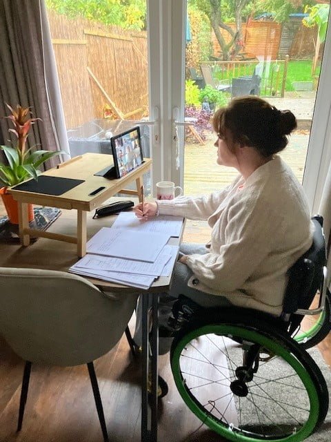 Woman sitting at her desk in her wheel chair, taking notes at home. 