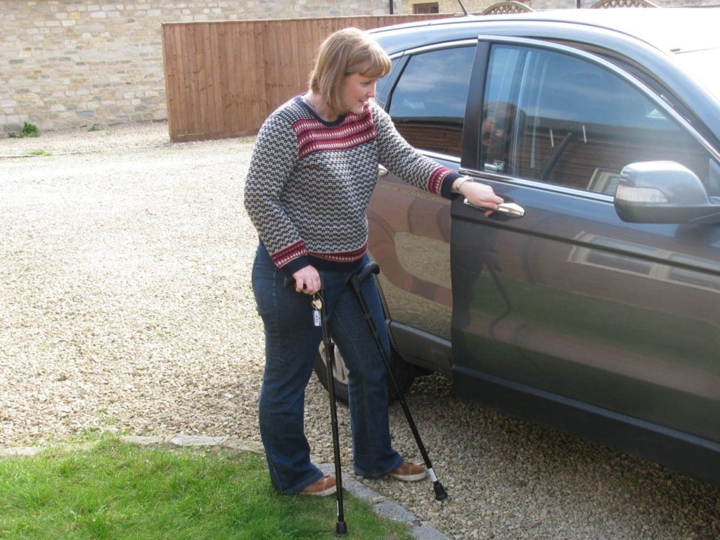 A woman who is able to walk with aids, opening a car