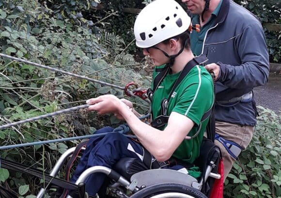 A young wheelchair user abseiling with a volunteer supporting