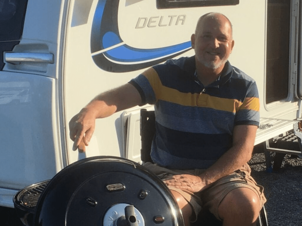 Steve, a wheelchair user, sat in front of his caravan, cooking on a BBQ