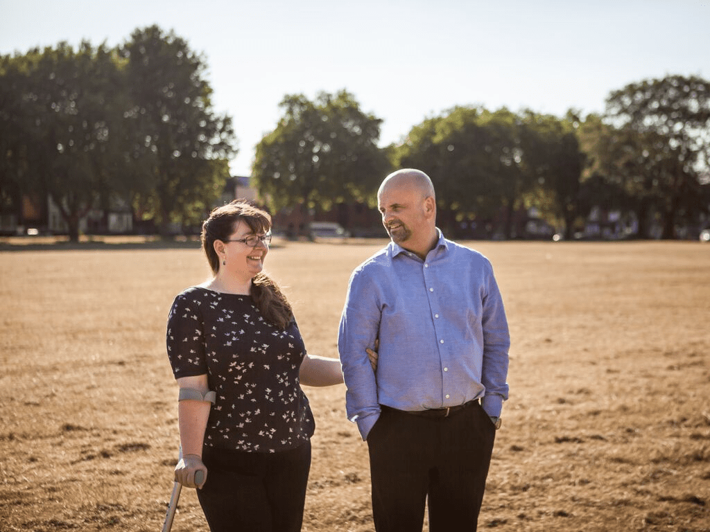 Chloe, a person with a spinal cord injury who can walk, standing in a field with her partner.