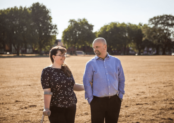 Chloe, a person with a spinal cord injury who can walk, standing in a field with her partner.