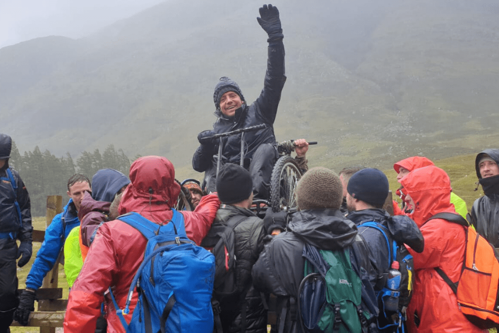 Andrew, a wheelchair user, being lifted over a fence during the Ben Nevis push