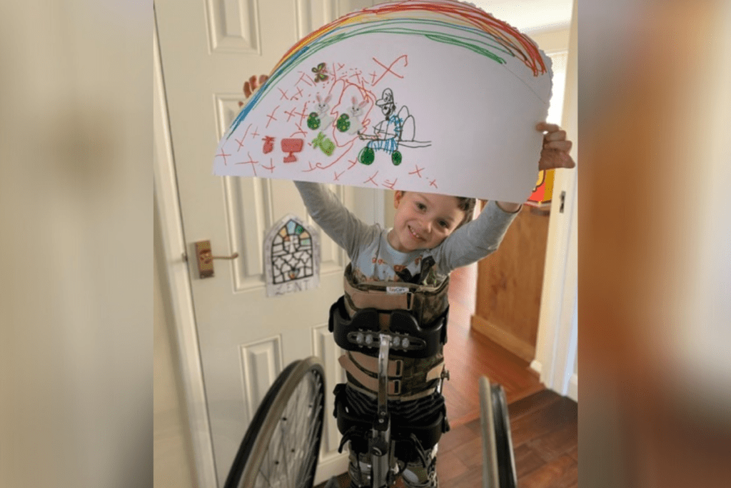 A young wheelchair user holding up a rainbow painting. this giving tuesday, you can help even more young people