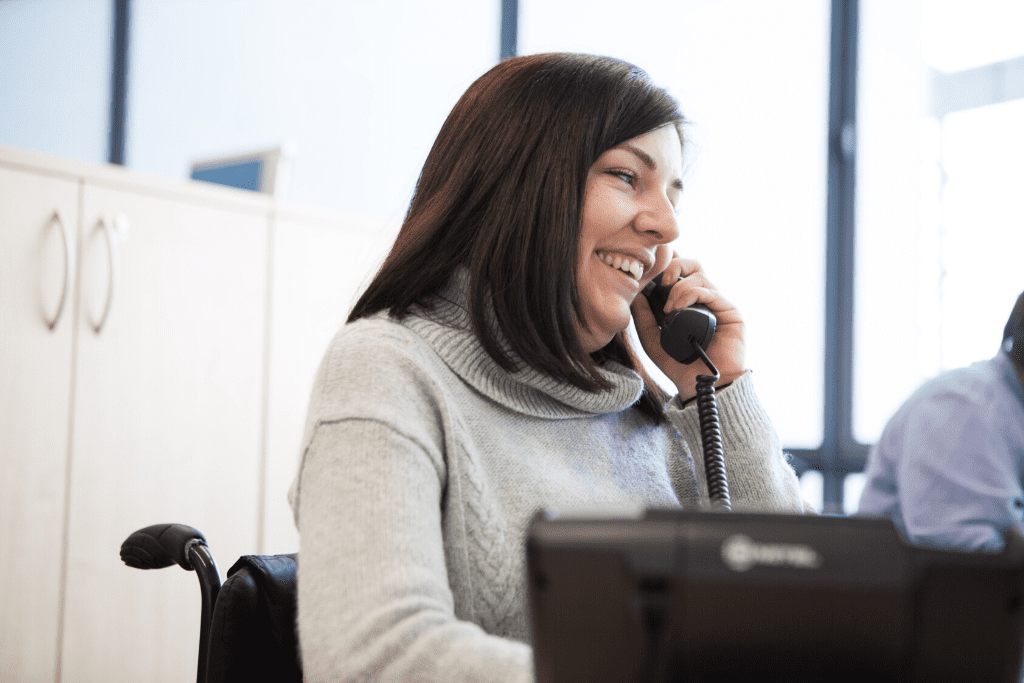 Ella, a wheelchair user who has a personal assistant, answering the phone in the Back Up office