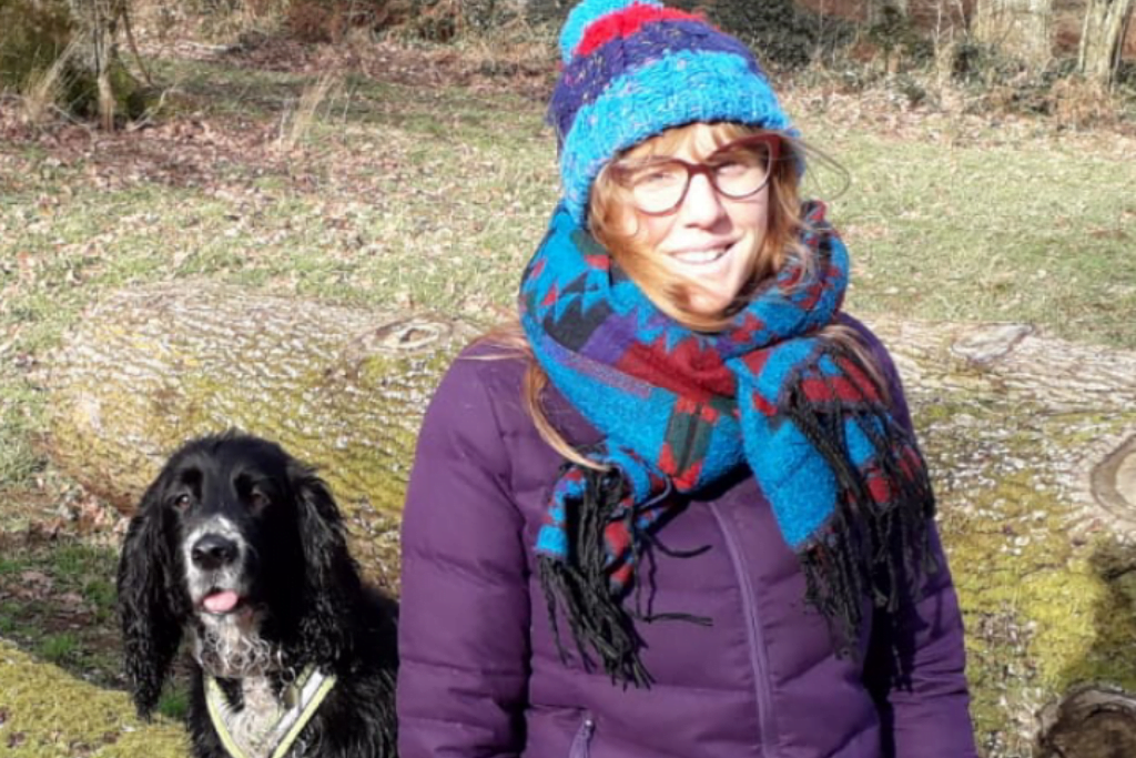 Holly, someone with a spinal cord injury who can walk without aids, sitting in a field with a dog