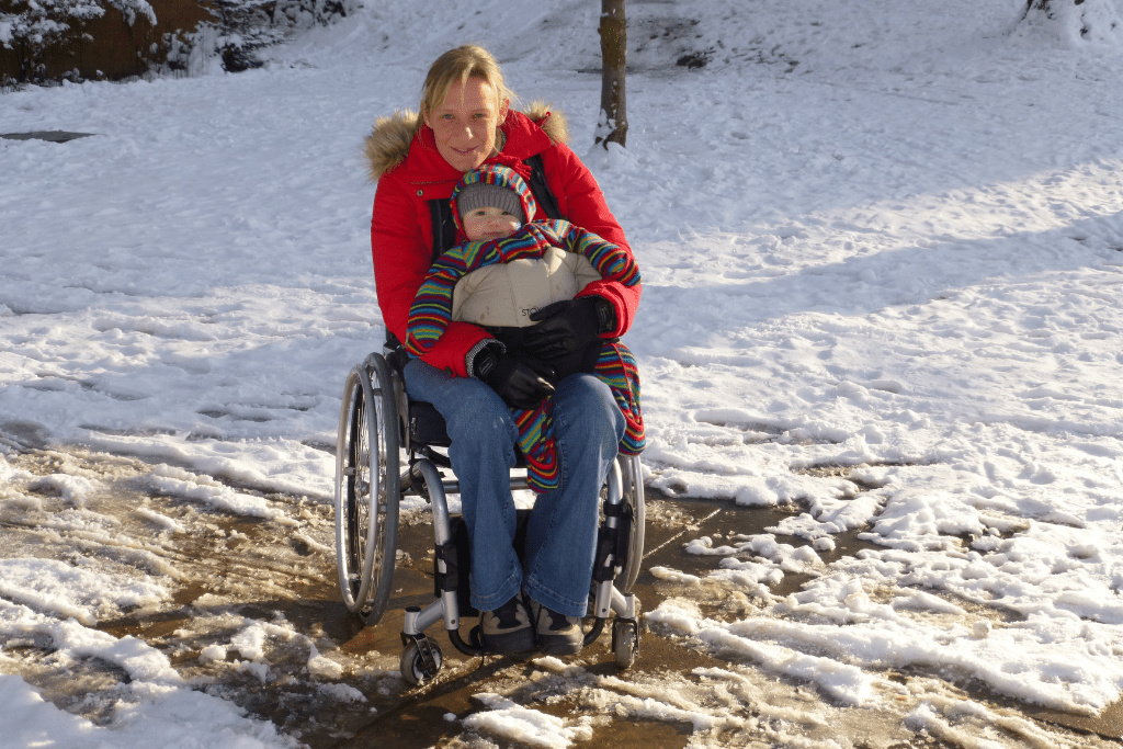 Clair, a spinal cord injured mum, holding her baby on her lap in a snowy field