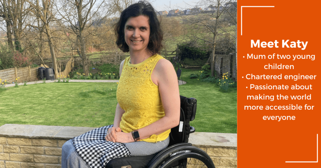 Katy is sitting in her wheelchair wearing a yellow t-shirt smiling in her garden. She has a C2-6 and T8 and T9 level incomplete spinal cord injury.