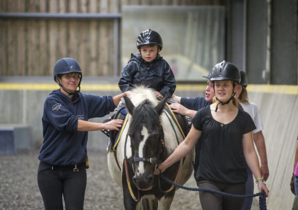 Young wheelchair user riding a horse with volunteers near